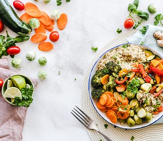 There is a bowl of vegertables on a white tablecloth. The veggies are chopped up into bite-sized pieces to fit nicely into a salad. There are lots of veggies scattered across the table.