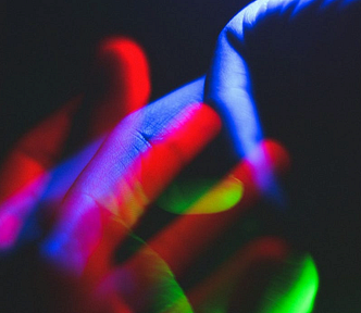 Hands intertwined, bathed in neon lights in blue, green, and red against a dark background