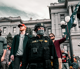 A picture of Trump supporters behind a cop, in front of a government building at a rally
