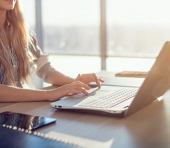 Woman blogging in spacious office using computer on her workplace. Female employee sitting, smiling, looking at camera.