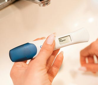 A woman’s hand holding a pregnancy test over a sink with the words ’not pregnant’ on the digital screen