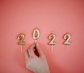 A white hand puts gold candles spelling out “2022” on a pink background.