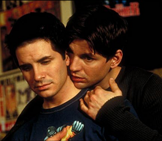A 20-something white man with dark hair being embraced by another 20-something white man with dark hair.