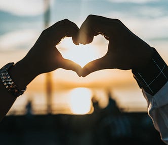 Sunrise, person forms heart with hands