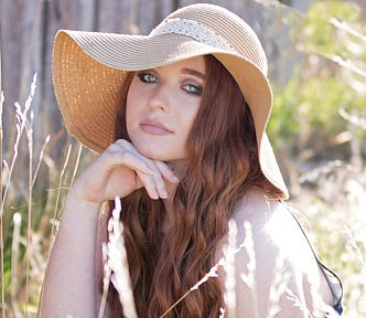 Young woman, brunette long hair, wears a floppy hat, surrounded by long grass, summer, countryside