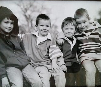 Black and white photograph of the author’s four sons sitting next to each other on a branch. Ages are approximately 3,4,6 and 8