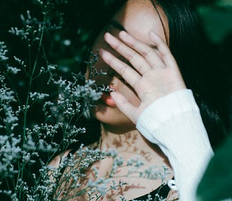 An Asian girl surrounded by flowers, covering her face from sunlight.