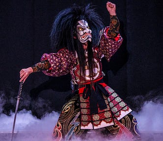 Traditionally dressed in costume, a man wearing an angry mask shakes his fist at the sky.