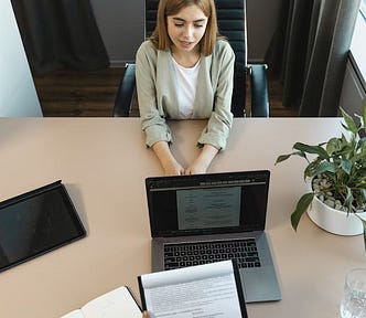 A woman speaking at a table with her hands on a table, while a person is holding a notepad with their resume on it (in addition to a laptop)