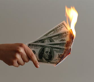 A hand holding four $100 bills that are on fire.