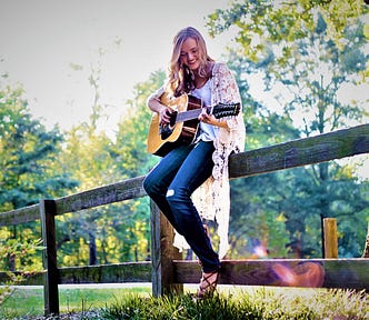 smiling girl with long blonde hair sitting on wooden fence and playing guitar