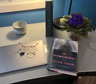In Memoriam, Alice Winn — book on desk next to laptop, eyeglasses, potted purple flowers