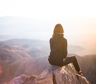 Woman sitting on the top of a mountain overlooking a body of water with islands.