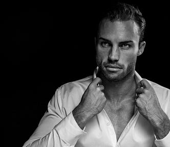 A monochrome portrait of a stereotypical dark romance male antagonist: a handsome, strong-jawed, well-muscled, designer-stubbled man, wearing a half-buttoned white shirt and staring sternly at a point just to the side of the camera.