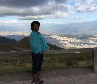 Aneisha standing in front of a mountain in Ecuador wearing a blue shawl.