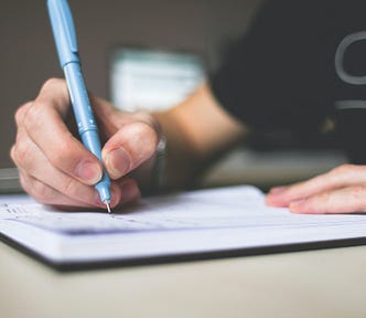 Person holding a pen while writing in a paper journal.