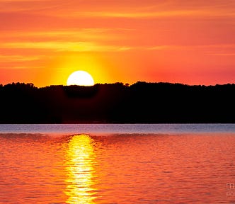 The sun rises over (and reflects off of) a calm lake in upstate New York.
