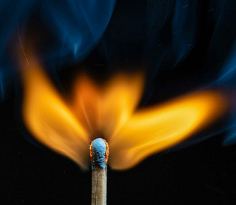 A closeup image of a lit match, blue smoke drifting up out of the frame