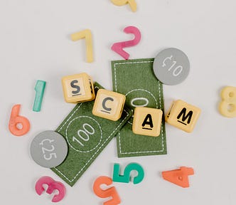 Photo of beads and trinkets spelling out the word ‘scam’. For the article, “Yes, IAPWE is a Scam”.