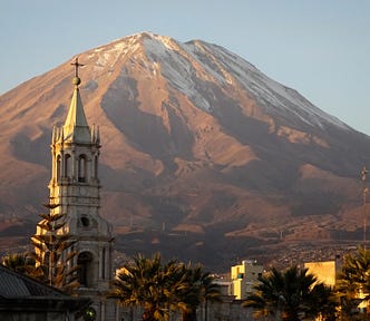 A church steeple infront of a large, slightly snow capped, mountain in Peru
