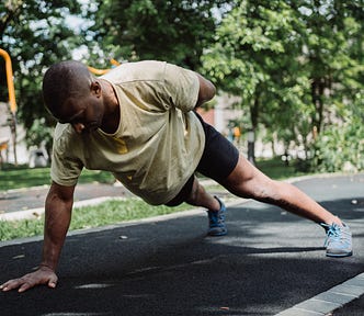 Black man in a light yellow shirt doing a one arm pushup