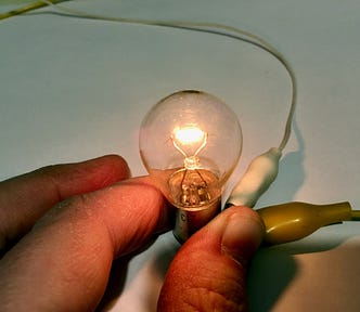 A hand holding wires on a low-voltage bulb