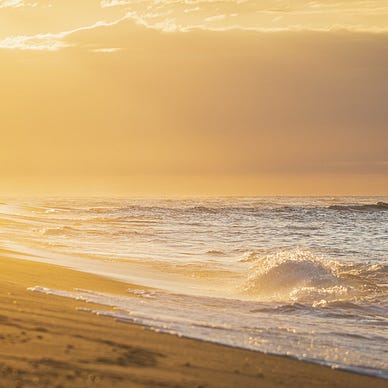 Sandy beach at sunrise. Gentle waves lapping at the shore against a backdrop of clouds