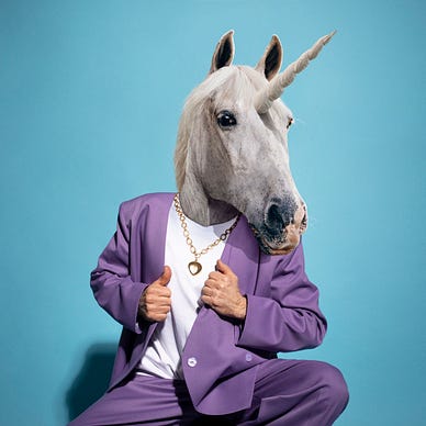 Person with a unicorn head mask wearing a purple suit against a blue background