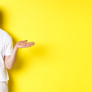 A clueless looking man in a white t shirt, shrugging and looking puzzled as if he has no idea what is going on. Bright yellow background.