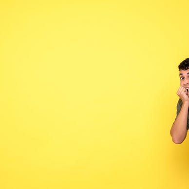 Man with his fists by his open mouth as if biting his nails. He looks very worried, but in an amused way. Bright yellow background