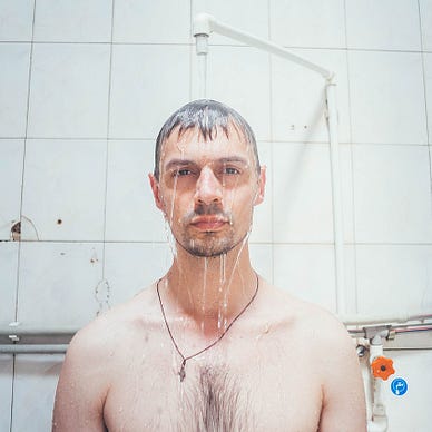 A man stands under a shower head and looks at the camera