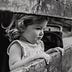 little girl wistfully looking through opening in wooden plank fence, a poet