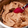 A red spatula is resting in the chocolate batter in a metal baking bowl