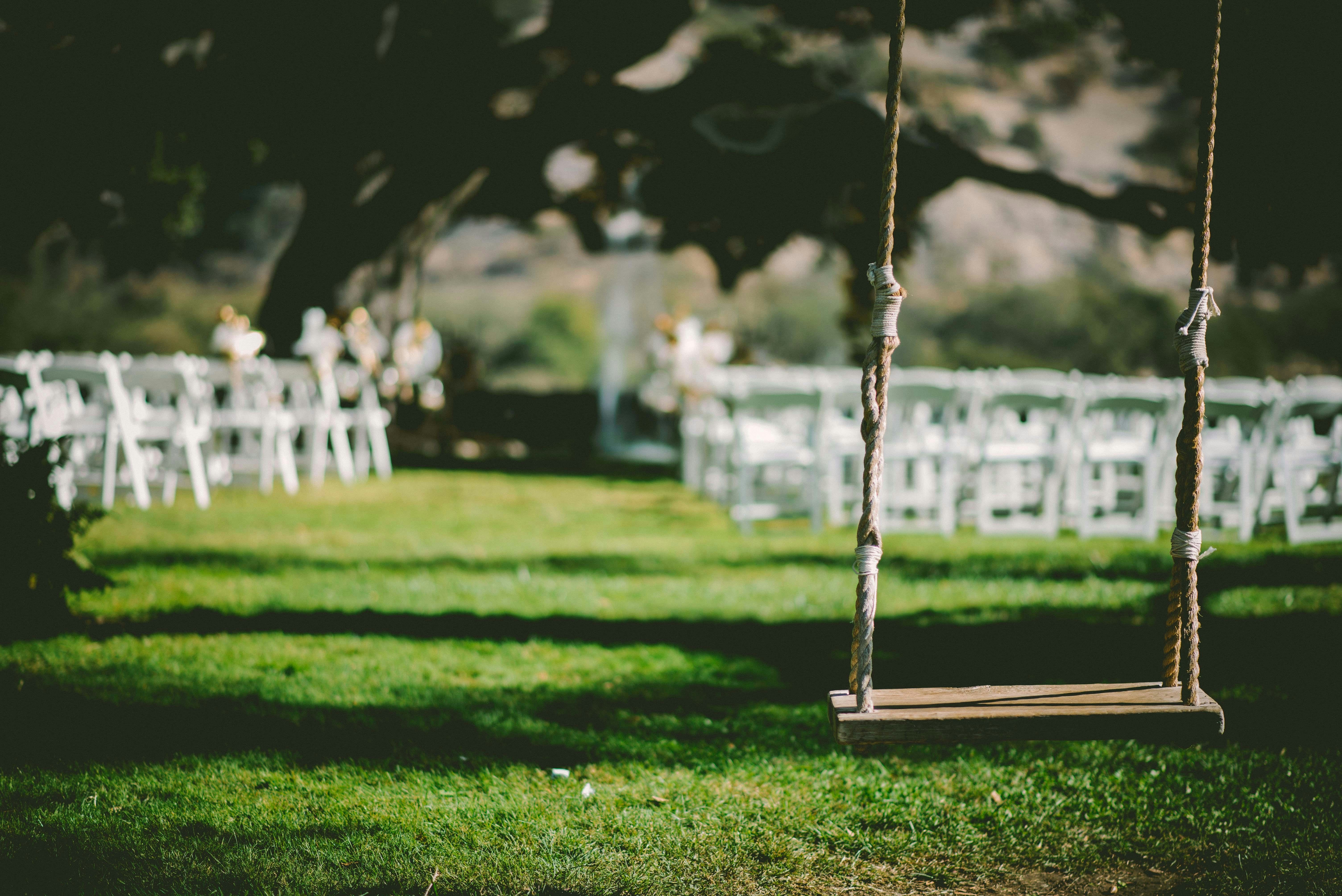 Wedding chairs set up out on a lawn with an empty swing in the foreground