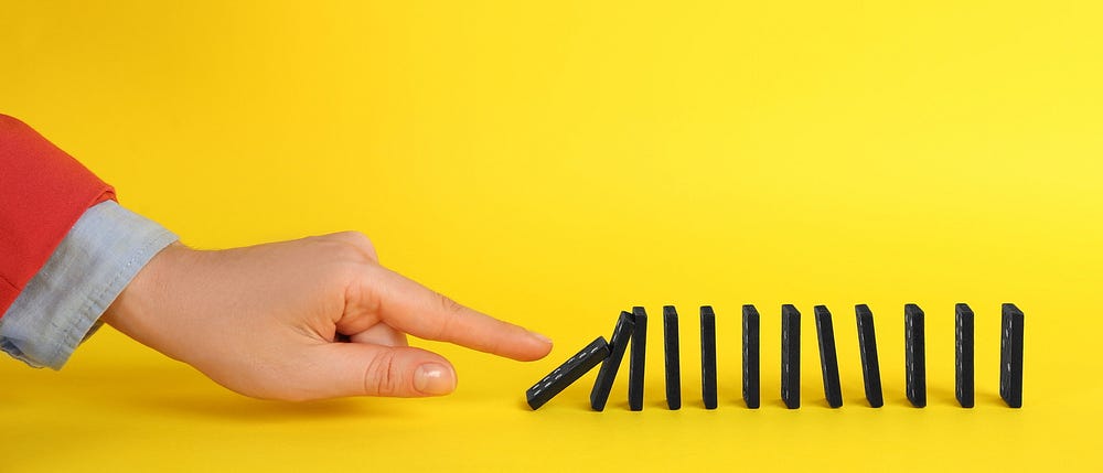 A hand with a pointer finger nudging the first domino brick in a line of others