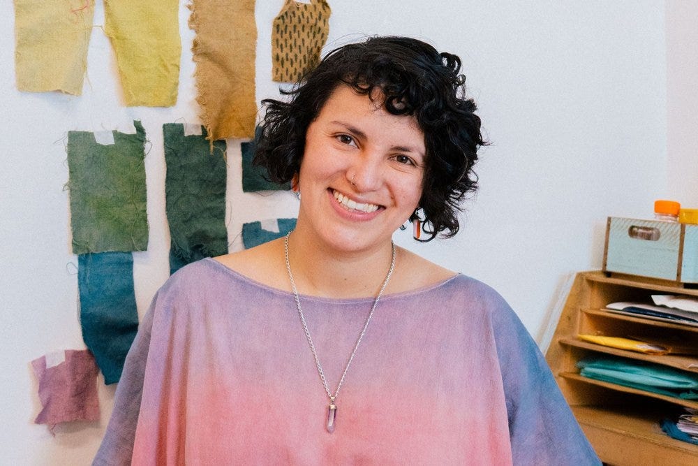 Natural dyer and designer Malú Colorin, founder of Talú natural dye house, stands in front of naturally-dyed textile samples taped to a wall [Credit: Talú via Reseed Podcast].