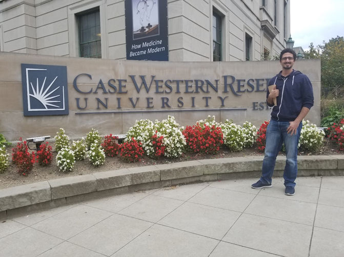Man posing next to a university sign.