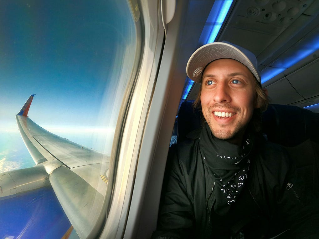 A guy smiling by the window seat in the airplane.