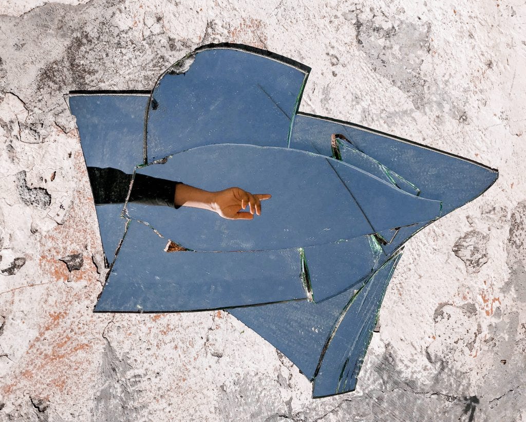 A collection of broken pieces of glass on the ground with a hand pointing to the right reflected in them. Pexels.com Bruno Pires
