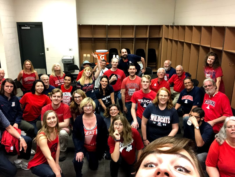 People wearing red sports shirt and taking a photo in a locker room.