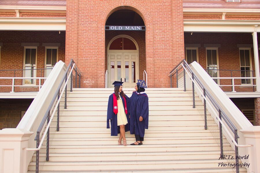 Two women on the steps with graduation robes.