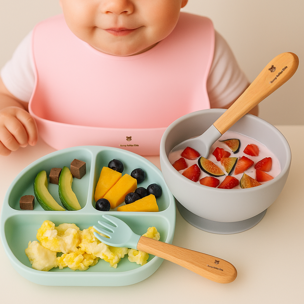a baby girl wearing a pink silicone bib from HUNNY BUBBA KIDSand eating fruits and other foods in non-slip and suction silicone bowl and plate also from Hunny Bubba Kids.