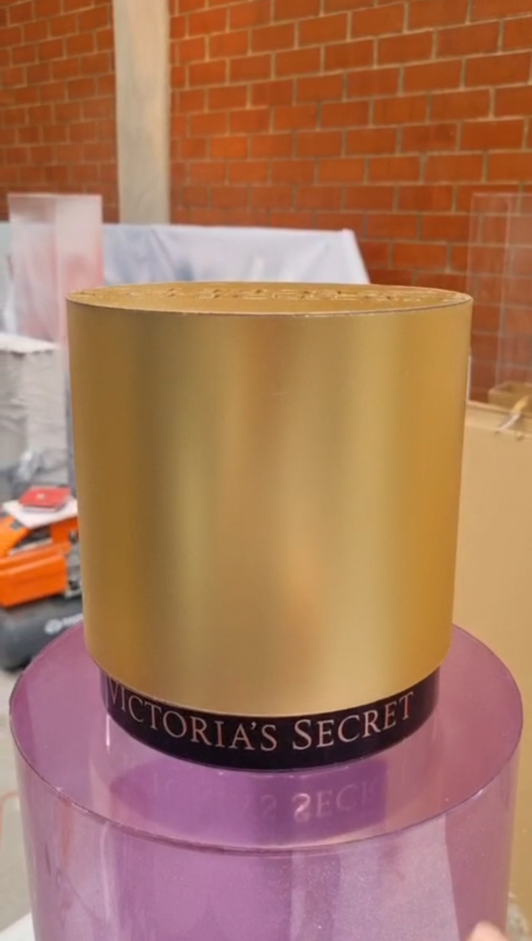 Cylindrical translucent pink and purple mica perfume display dummies with matte gold caps and central pink labels shown inside a workshop.
