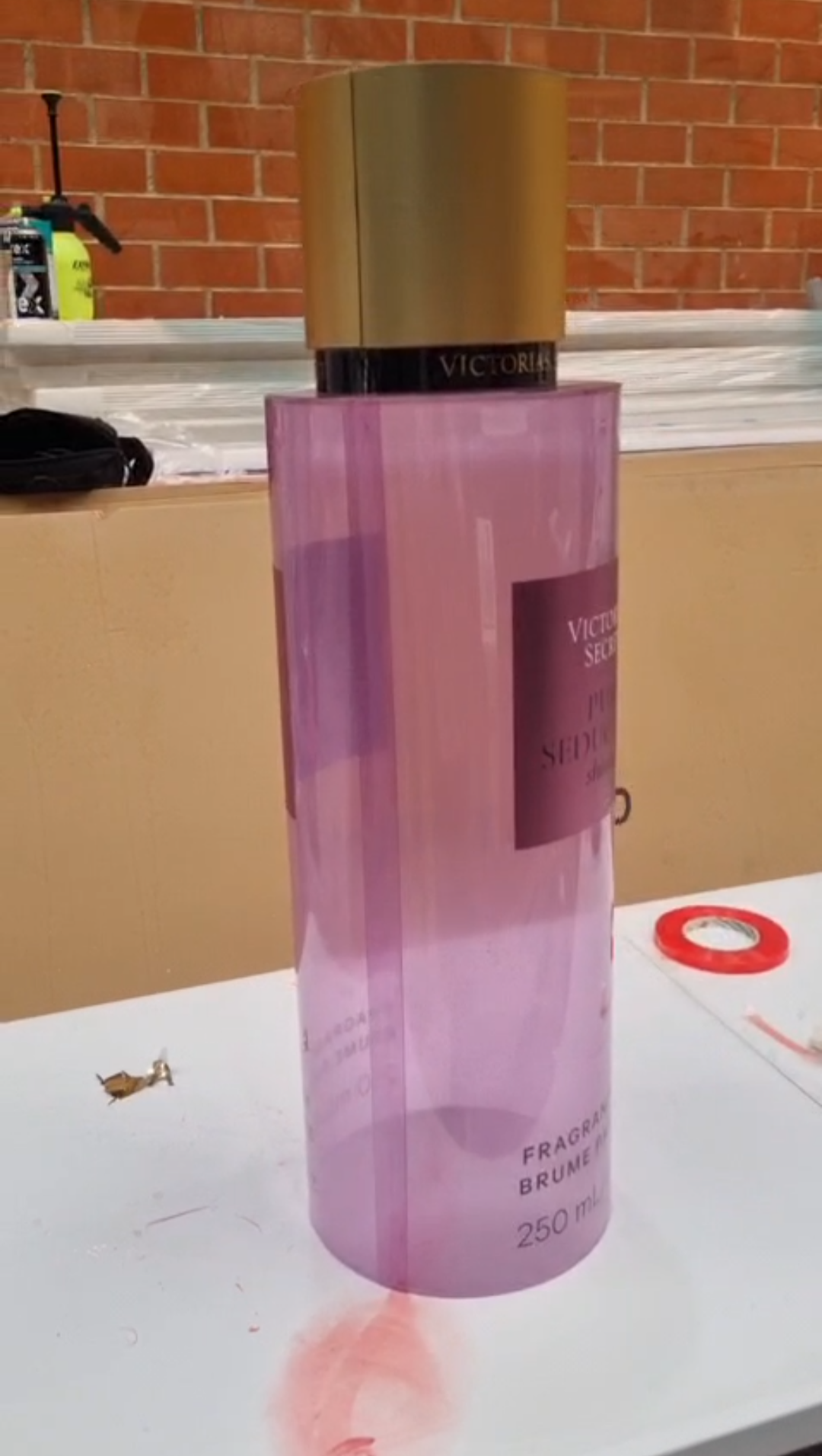 Cylindrical translucent pink and purple mica perfume display dummies with matte gold caps and central pink labels shown inside a workshop.