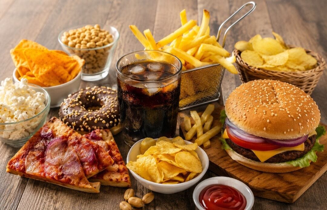 Assorted fast foods including burger, fries, pizza, chips, donut, and soft drink that may trigger gastric and acidity problems.