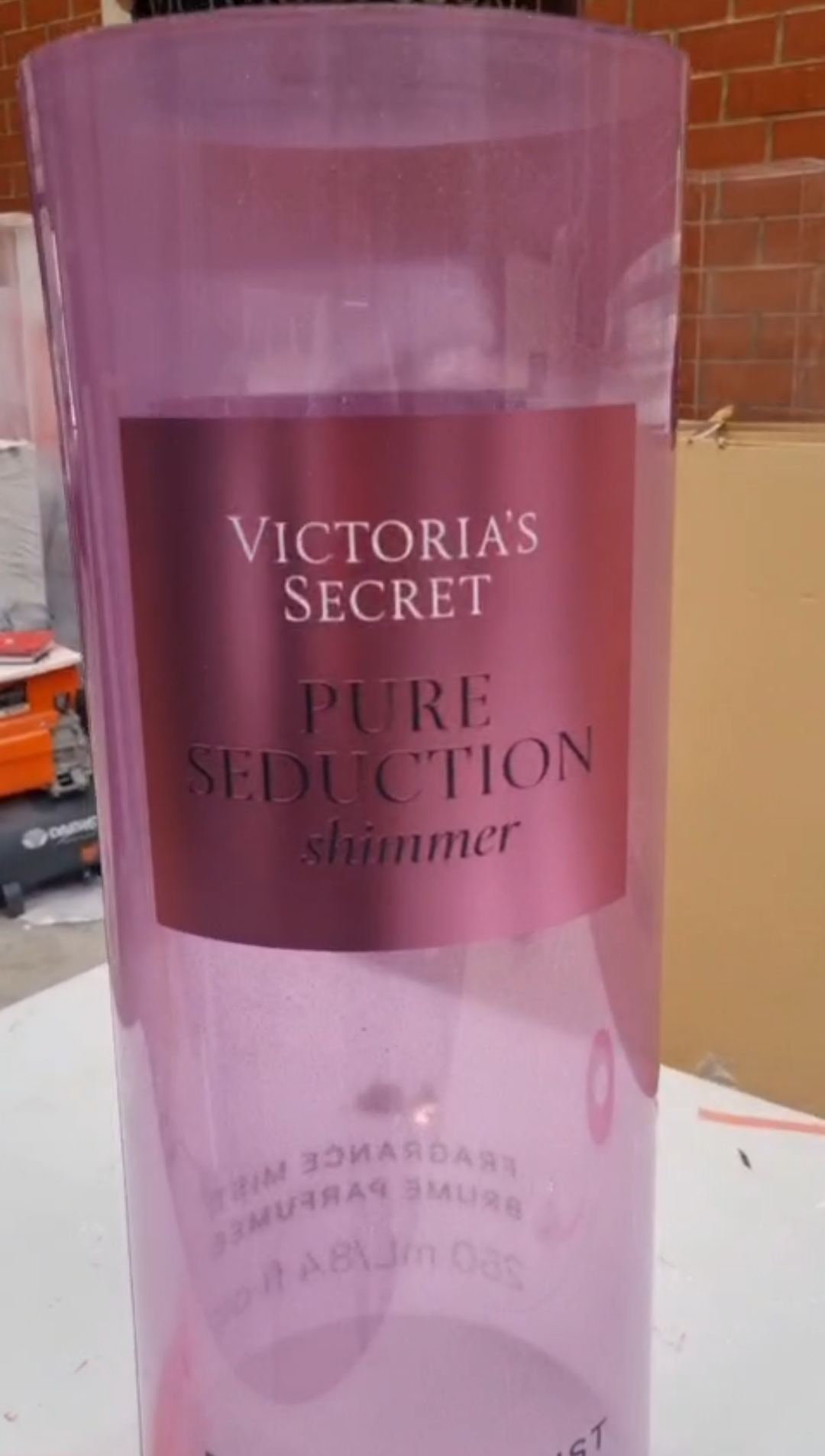 Cylindrical translucent pink and purple mica perfume display dummies with matte gold caps and central pink labels shown inside a workshop.