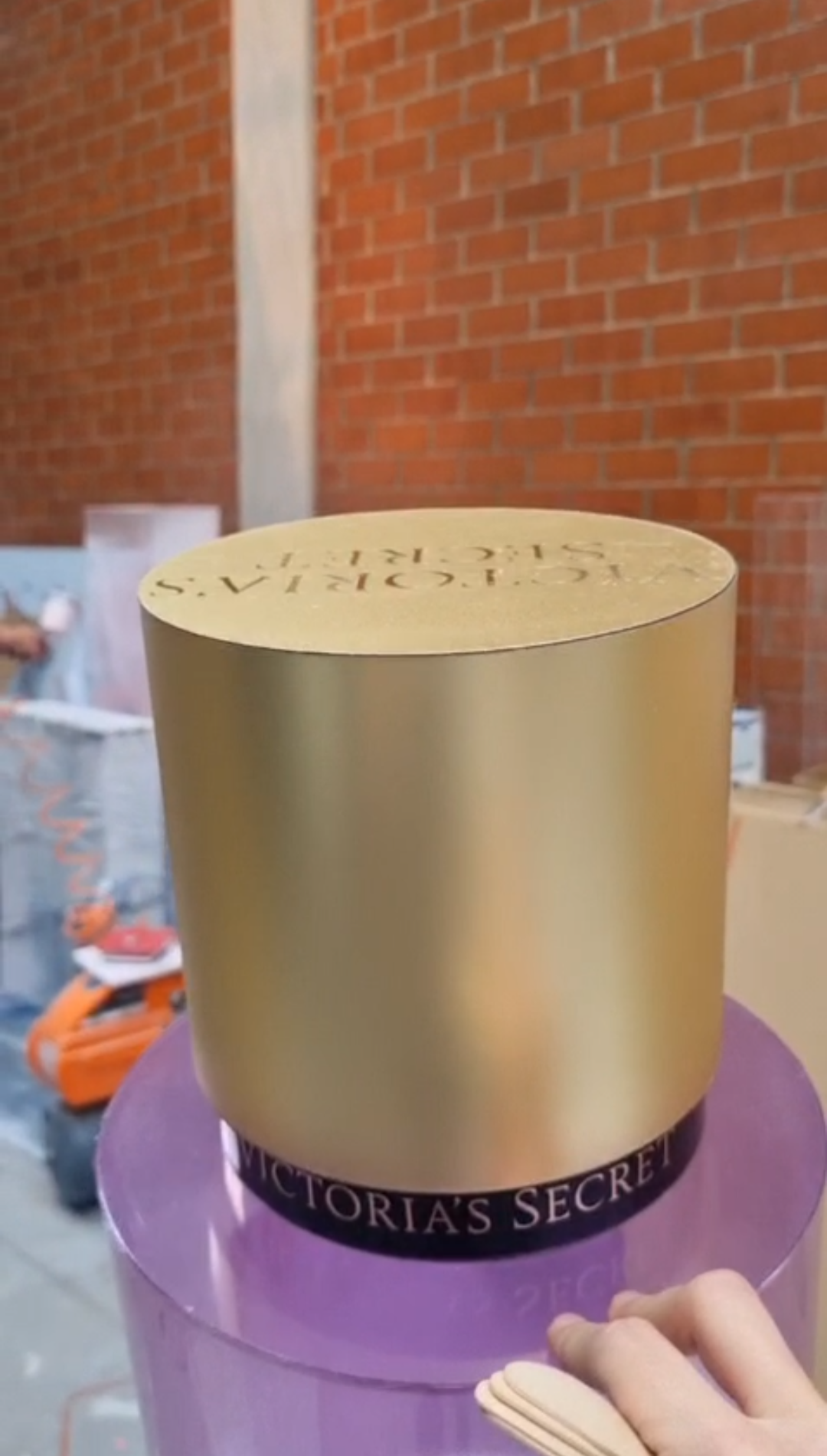 Cylindrical translucent pink and purple mica perfume display dummies with matte gold caps and central pink labels shown inside a workshop.