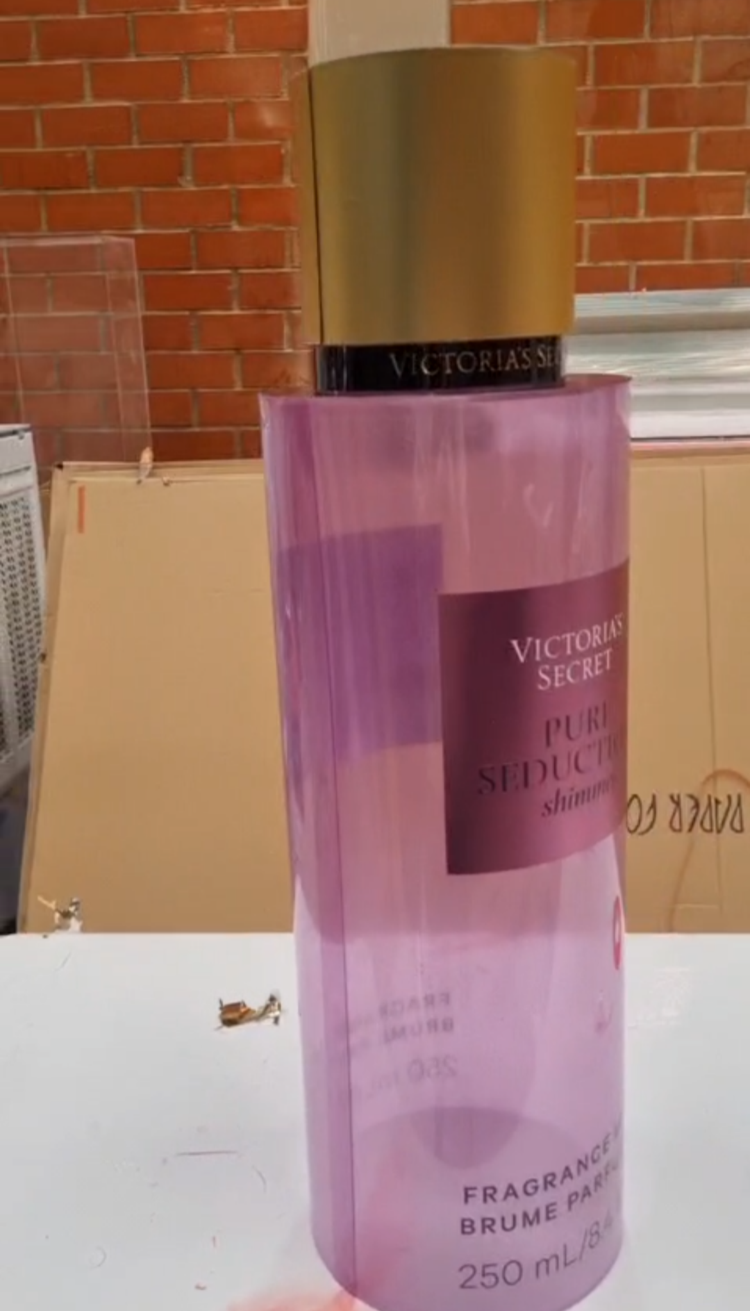 Cylindrical translucent pink and purple mica perfume display dummies with matte gold caps and central pink labels shown inside a workshop.