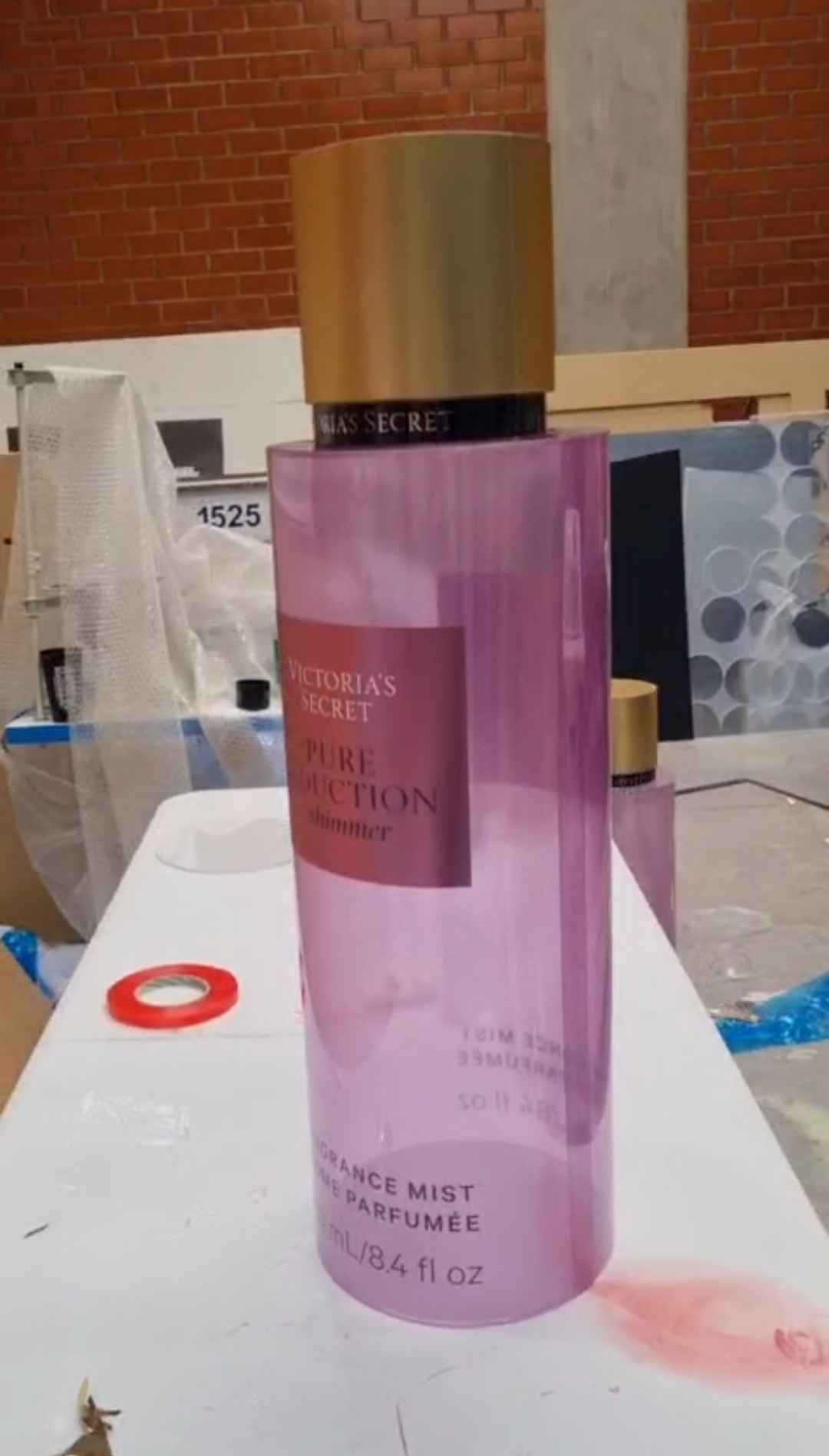 Cylindrical translucent pink and purple mica perfume display dummies with matte gold caps and central pink labels shown inside a workshop.