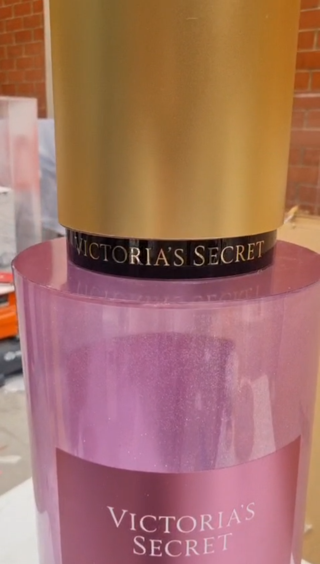 Cylindrical translucent pink and purple mica perfume display dummies with matte gold caps and central pink labels shown inside a workshop.